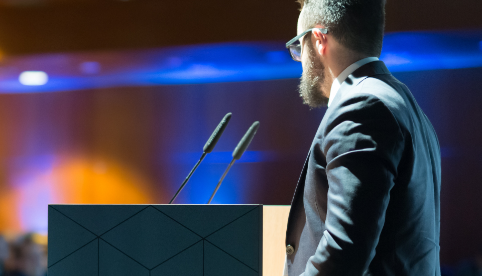 Palestrante conduzindo uma apresentação em um evento corporativo, com foco na integração entre conteúdo e destino